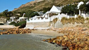 A coastal area with white buildings, a rocky beach, and a mountainous backdrop. - Westbank (Cape Town)