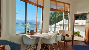 A dining area with a table and chairs, large windows with a view of the sea and mountains, and a balcony with a view of the sea. - Westbank (Cape Town)