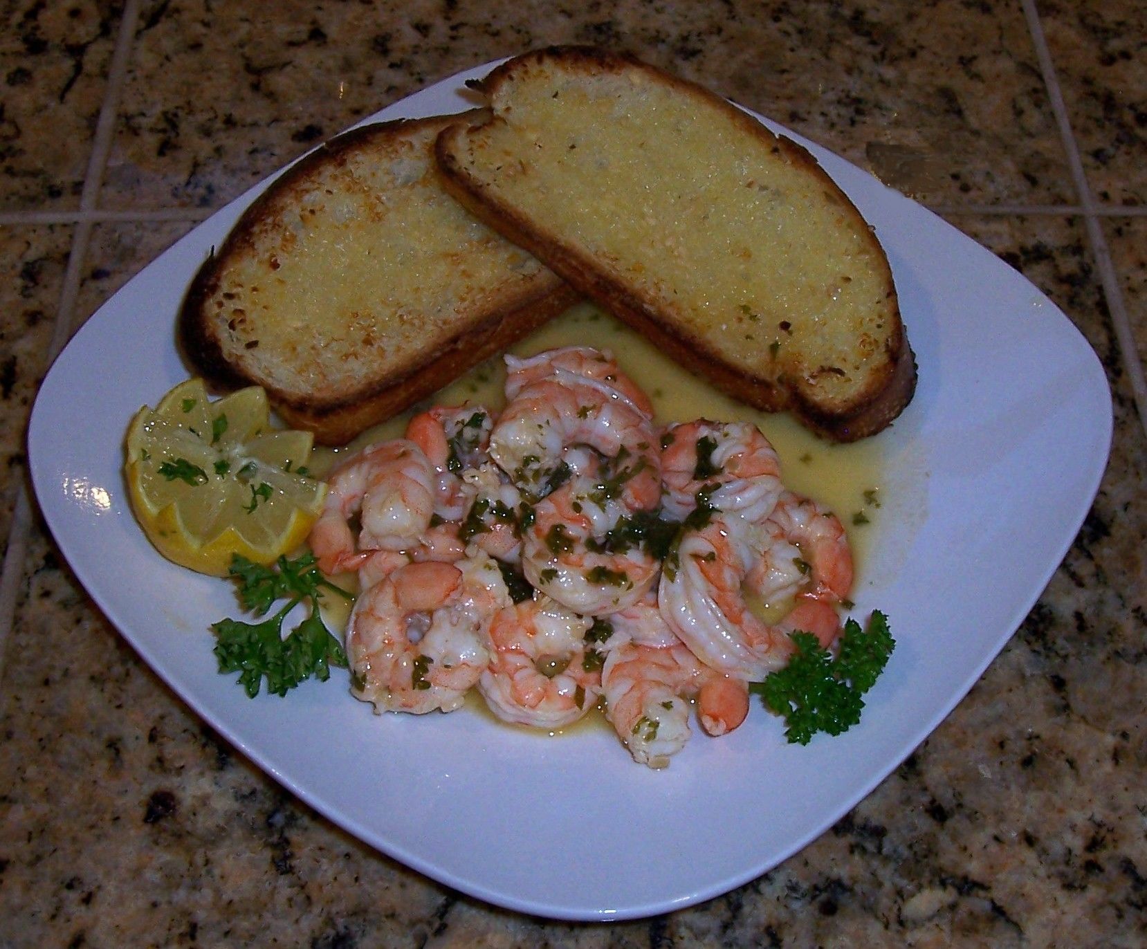 Une assiette de crevettes, garnie de tranches de citron et de persil, accompagnée de pain grillé.