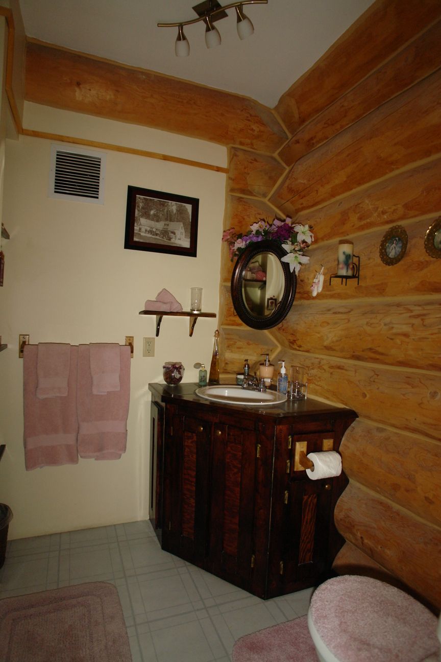 A bathroom with wooden walls, a sink, a mirror, and a toilet.