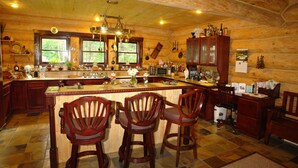 A wooden cabin-style kitchen with a large island, bar stools, and a variety of kitchen appliances and decorations. - The Garrison Inn a Montana Bed & Breakfast (Kalispell)