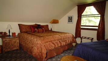 A bedroom with a large bed, a small table, a nightstand, a window with curtains, and a picture on the wall.