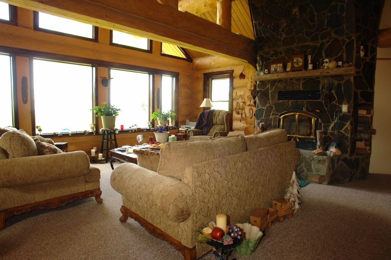 A cozy living room with a stone fireplace, large windows, and a mix of furniture including sofas and a coffee table.