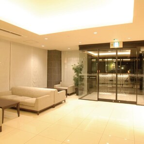 A modern lobby with a sofa, chairs, a small table, and a glass door leading to another area.