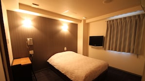 Une chambre d’hôtel avec un lit, un bureau, une chaise, une télévision et une fenêtre avec des rideaux.