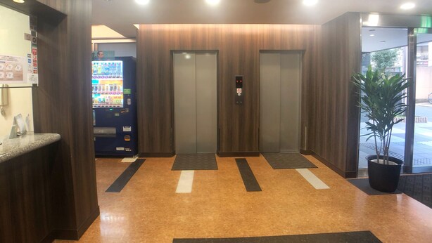 Un espace d’accueil avec un distributeur automatique, deux ascenseurs et une plante en pot.