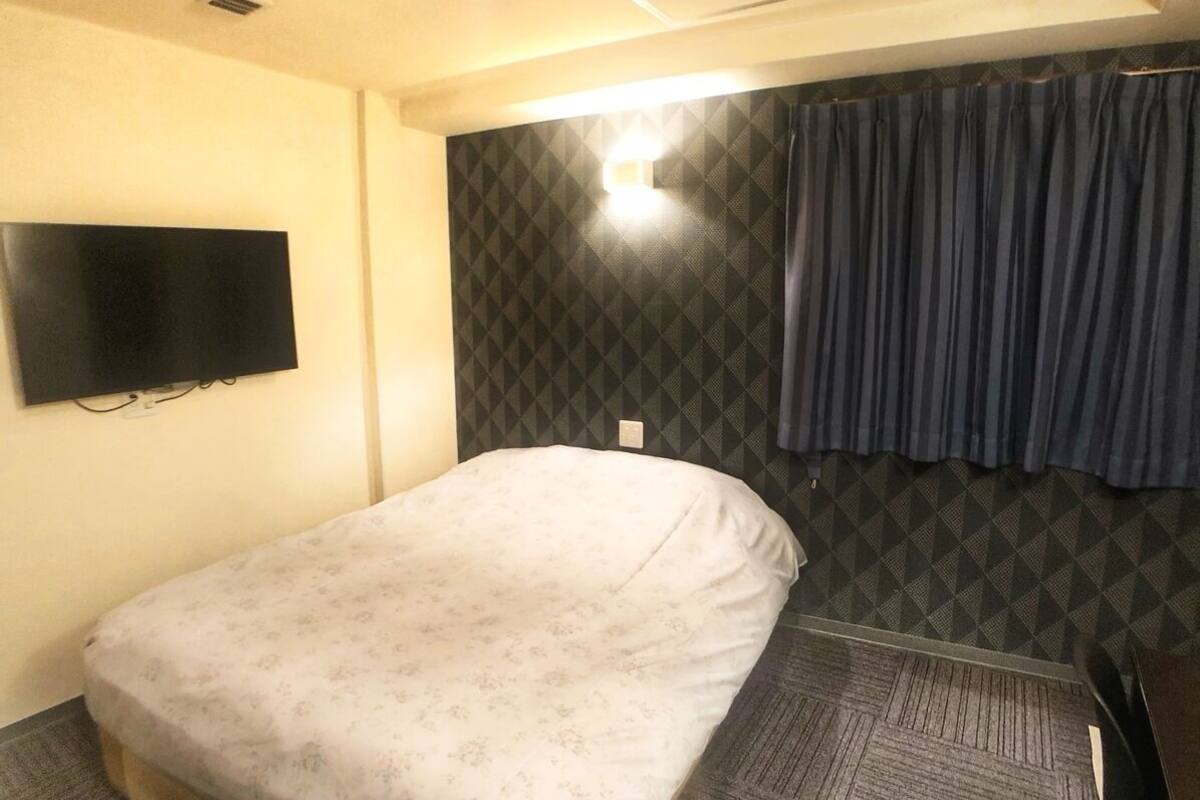 Quarto de hotel com uma cama, televisão de tela plana na parede, parede estampada e cortina.