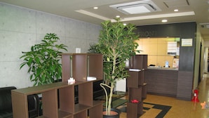 Un espace d’accueil comprenant un comptoir de réception, une plante en pot et un coin salon avec des chaises.
