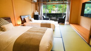 A hotel room with two beds, a TV, a window with a view of greenery, and a small table with chairs. - Yufuin Floral Village Hotel (Yufu)