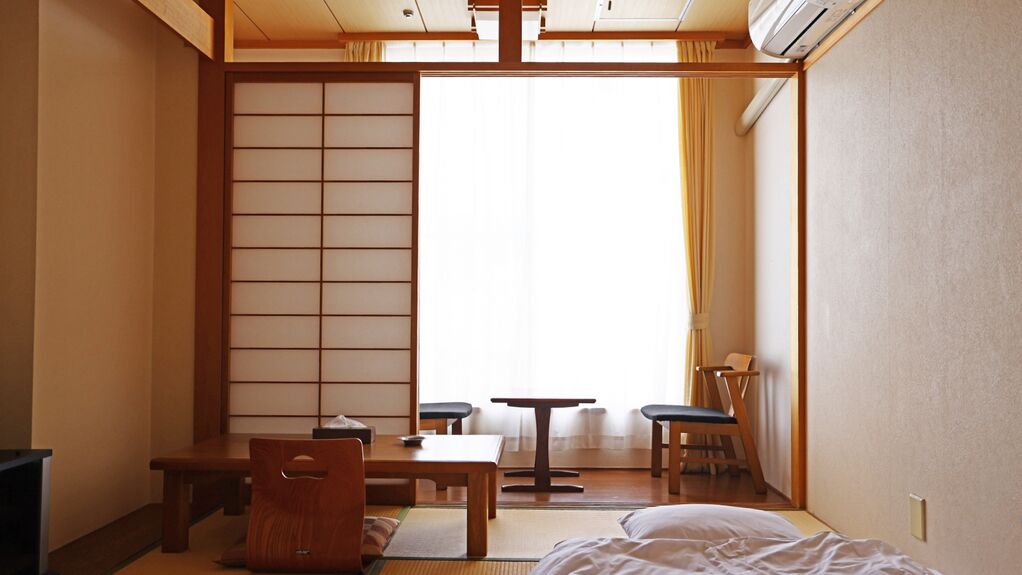 A traditional Japanese room with tatami flooring, a low table, a chair, and a bed.