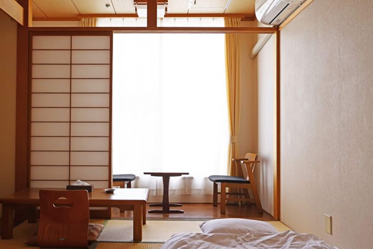 Una habitación japonesa tradicional con suelo de tatami, una mesa baja, una silla y una cama.