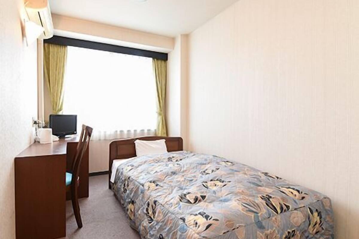 Une pièce comprenant un lit, un bureau, une chaise, une fenêtre avec des rideaux et une lampe fixée au mur.