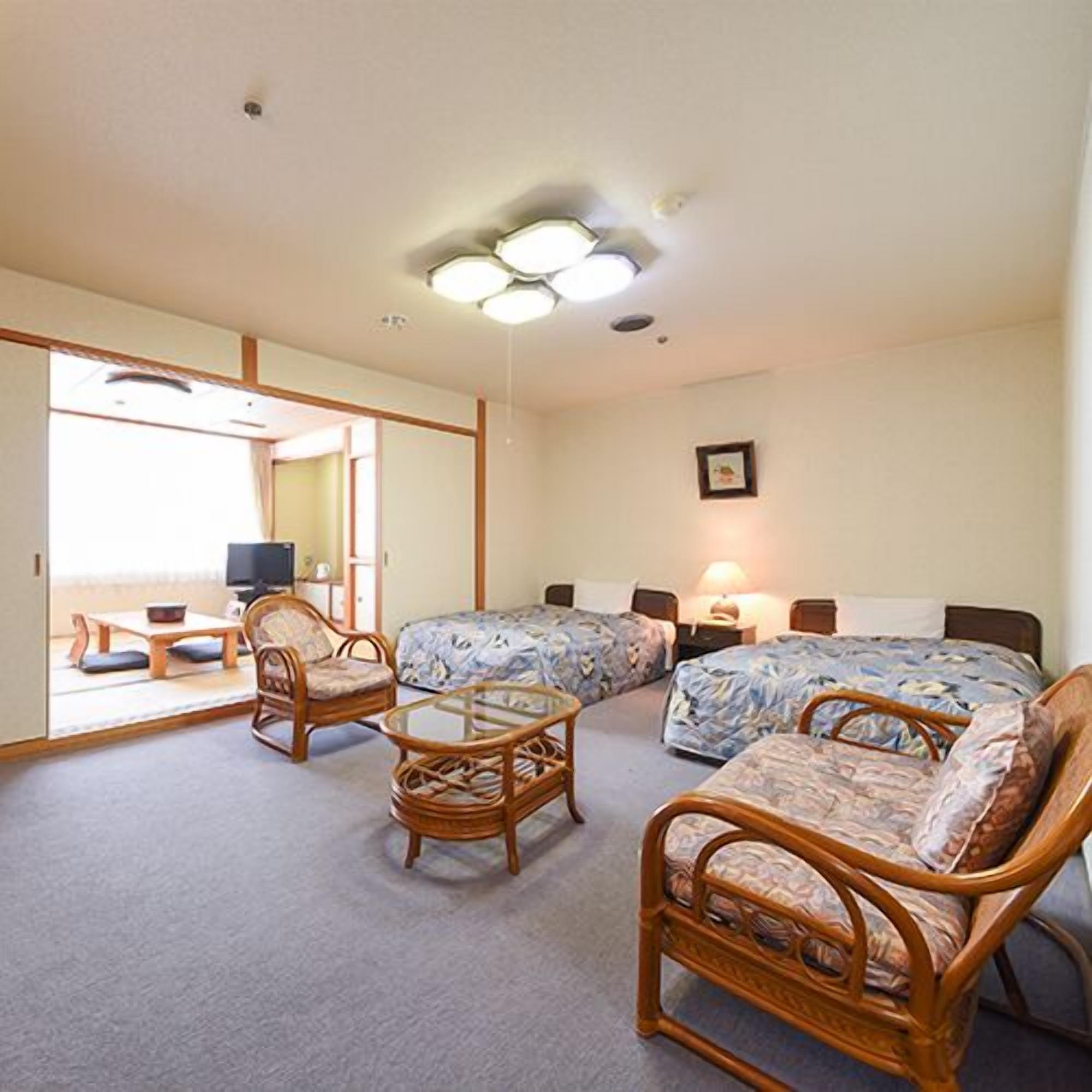 Ein Zimmer mit zwei Betten, einem Schlafsofa, einem Sessel, einem kleinen Tisch und einem Fernseher.