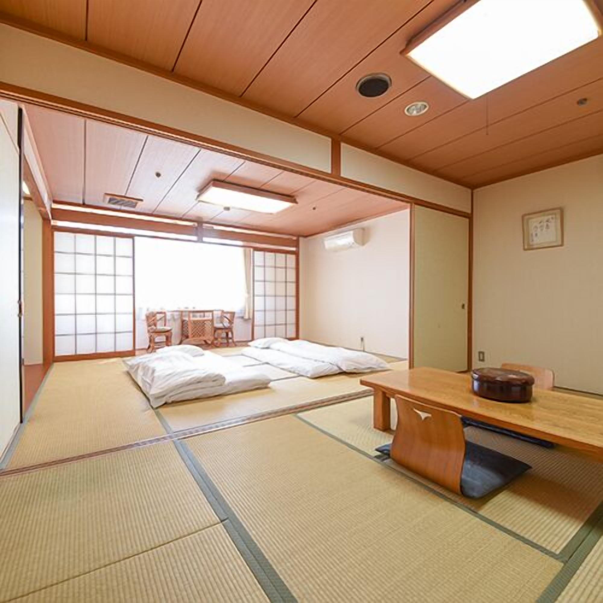 Ein traditioneller japanischer Raum mit Tatami-Böden, einem niedrigen Holztisch und einem Bett mit weißer Bettwäsche.