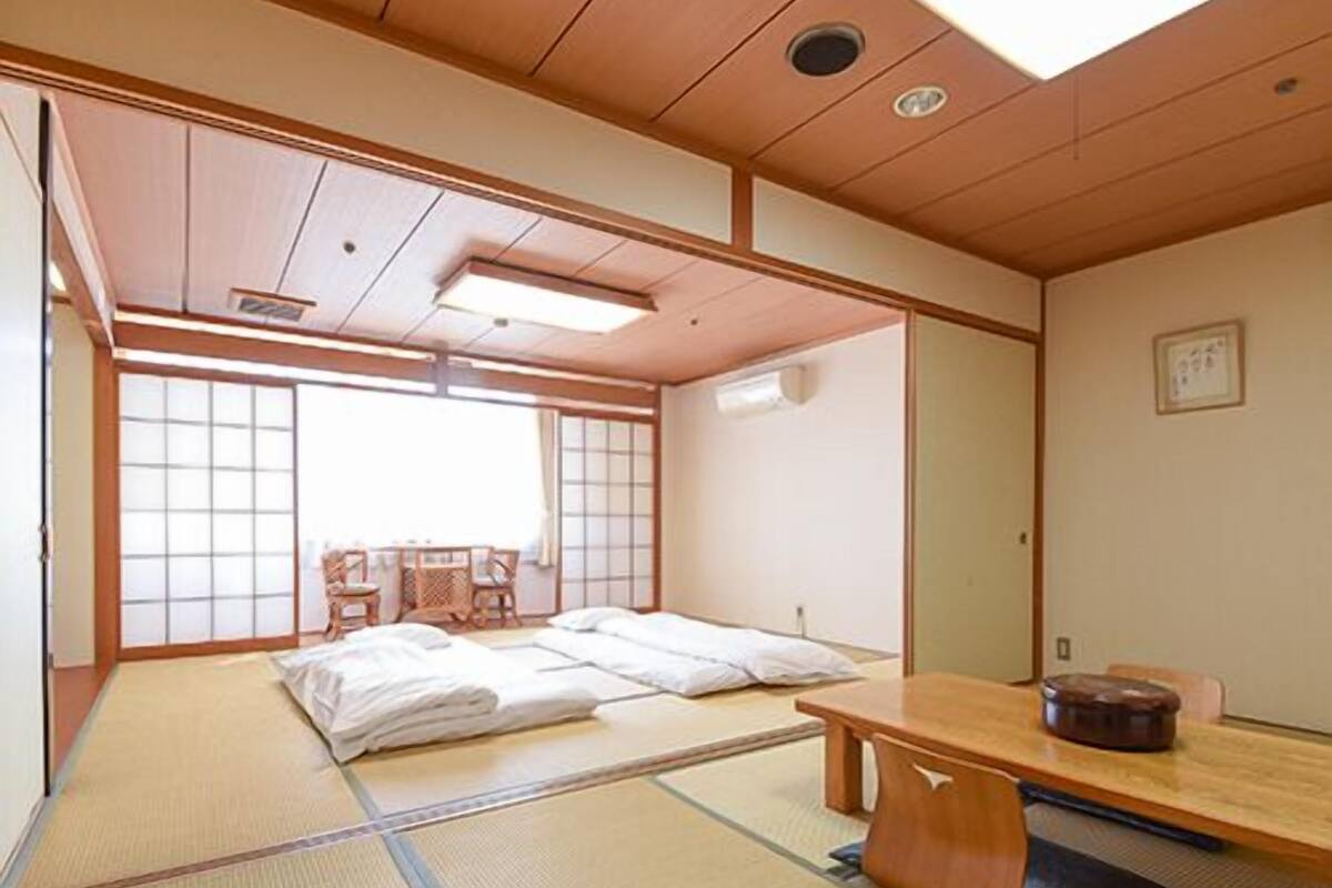 Une pièce de style japonais traditionnel, avec un sol recouvert de tatamis, une petite table en bois et un lit avec une literie blanche.