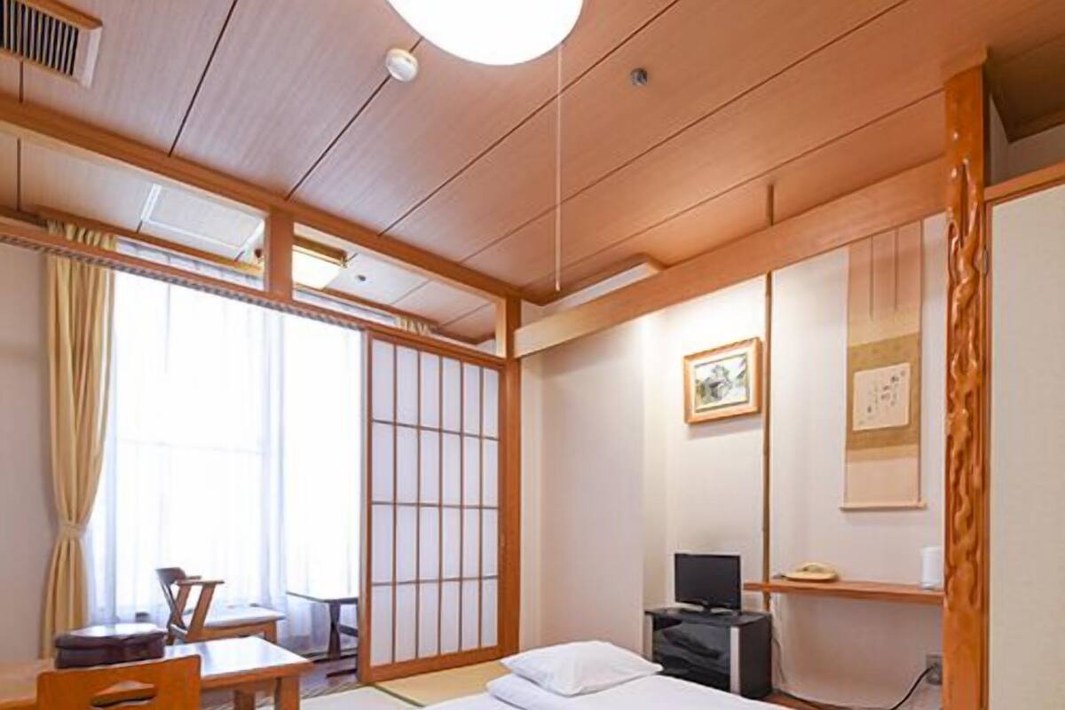 Une pièce de style japonais traditionnel, avec un sol recouvert de tatamis, un lit bas, un bureau avec une chaise et des portes coulissantes en papier de riz (shoji).