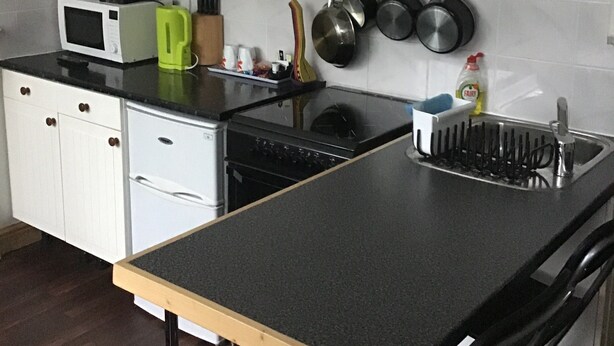 A kitchen with a microwave, toaster, kettle, stove, and hanging pots. - Number 16 at The Hub (Swansea)