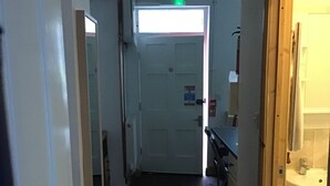 A narrow hallway with wooden flooring, a white door at the end, and a sink visible through an open door on the right. - Number 16 at The Hub (Swansea)
