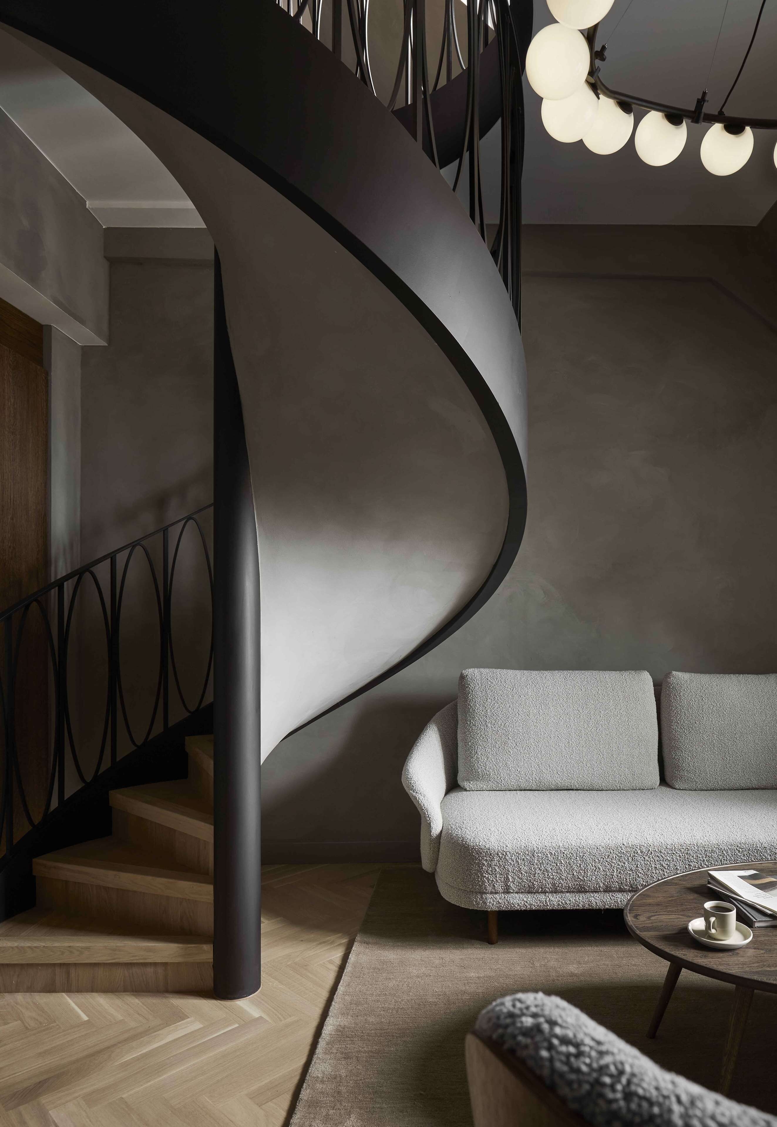 A modern interior with a curved staircase, a grey sofa, and a round coffee table.