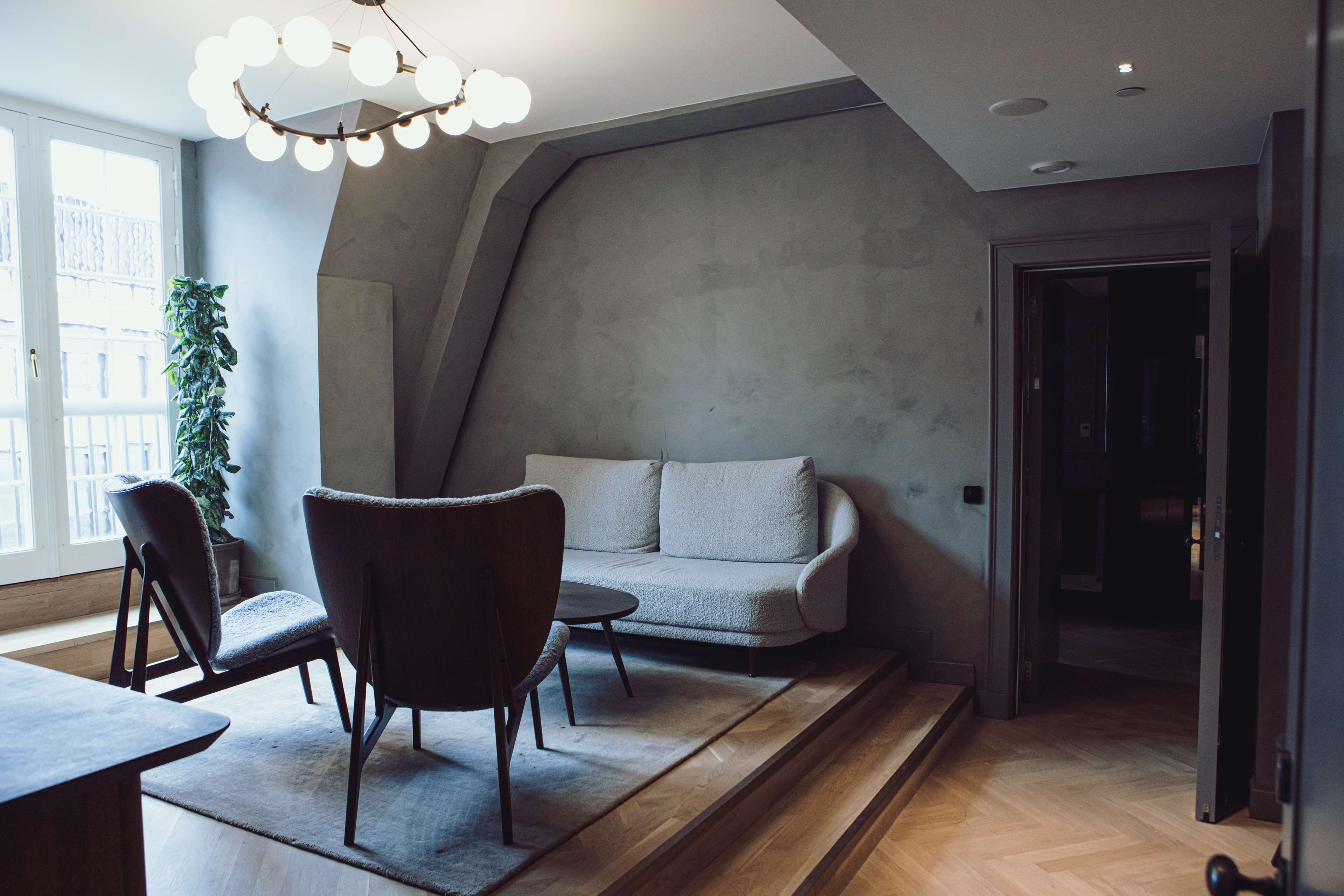 A modern living room with a sofa, two armchairs, a coffee table, and a potted plant.