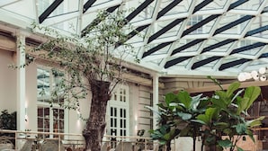 A modern indoor space with a high ceiling, a large tree, and seating areas. - Villa Copenhagen (Copenhagen)
