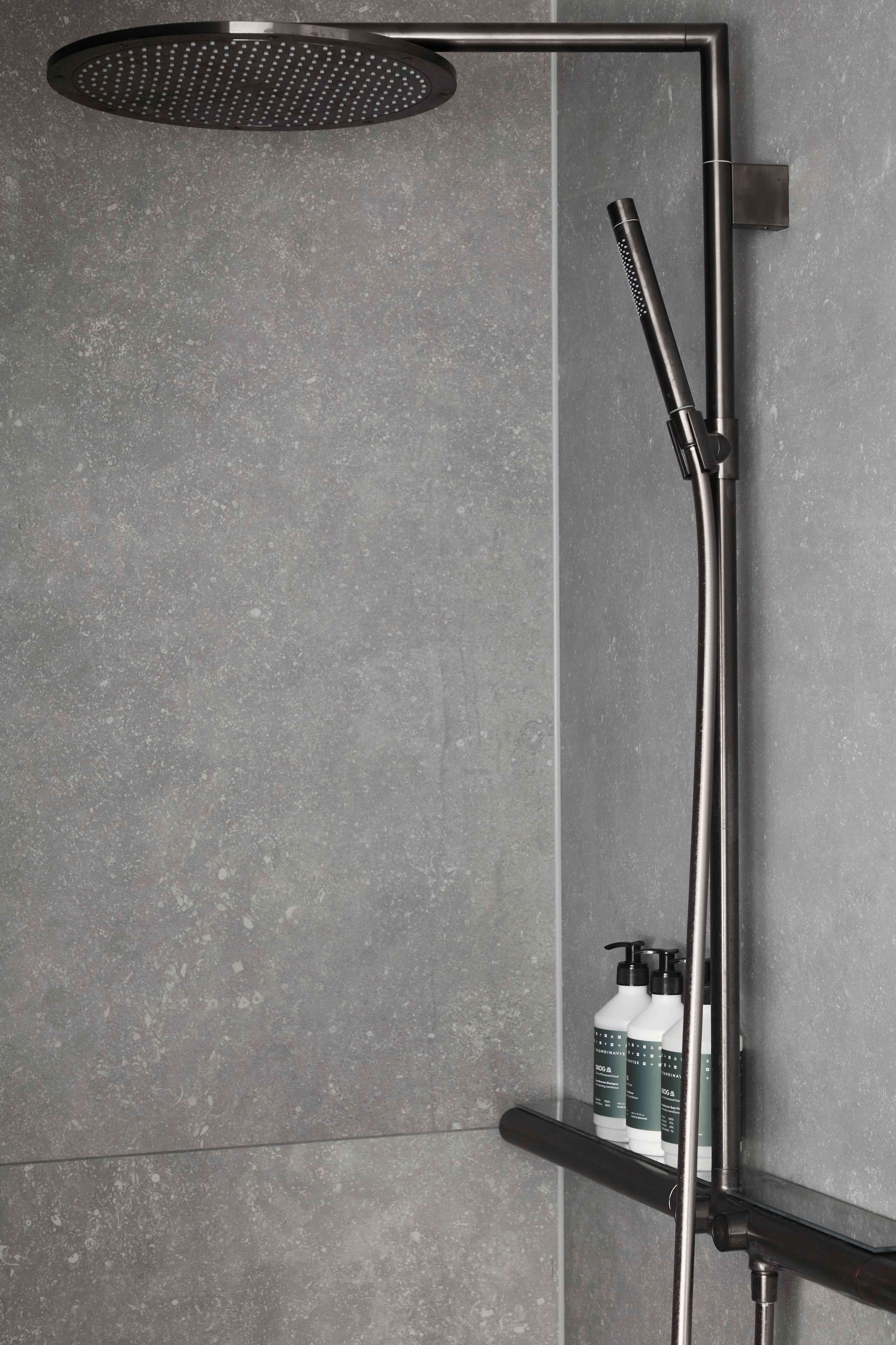 A modern shower with a round head, a handheld showerhead, and a shelf with bottles.