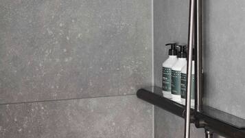 A modern shower with a round head, a handheld showerhead, and a shelf with bottles.