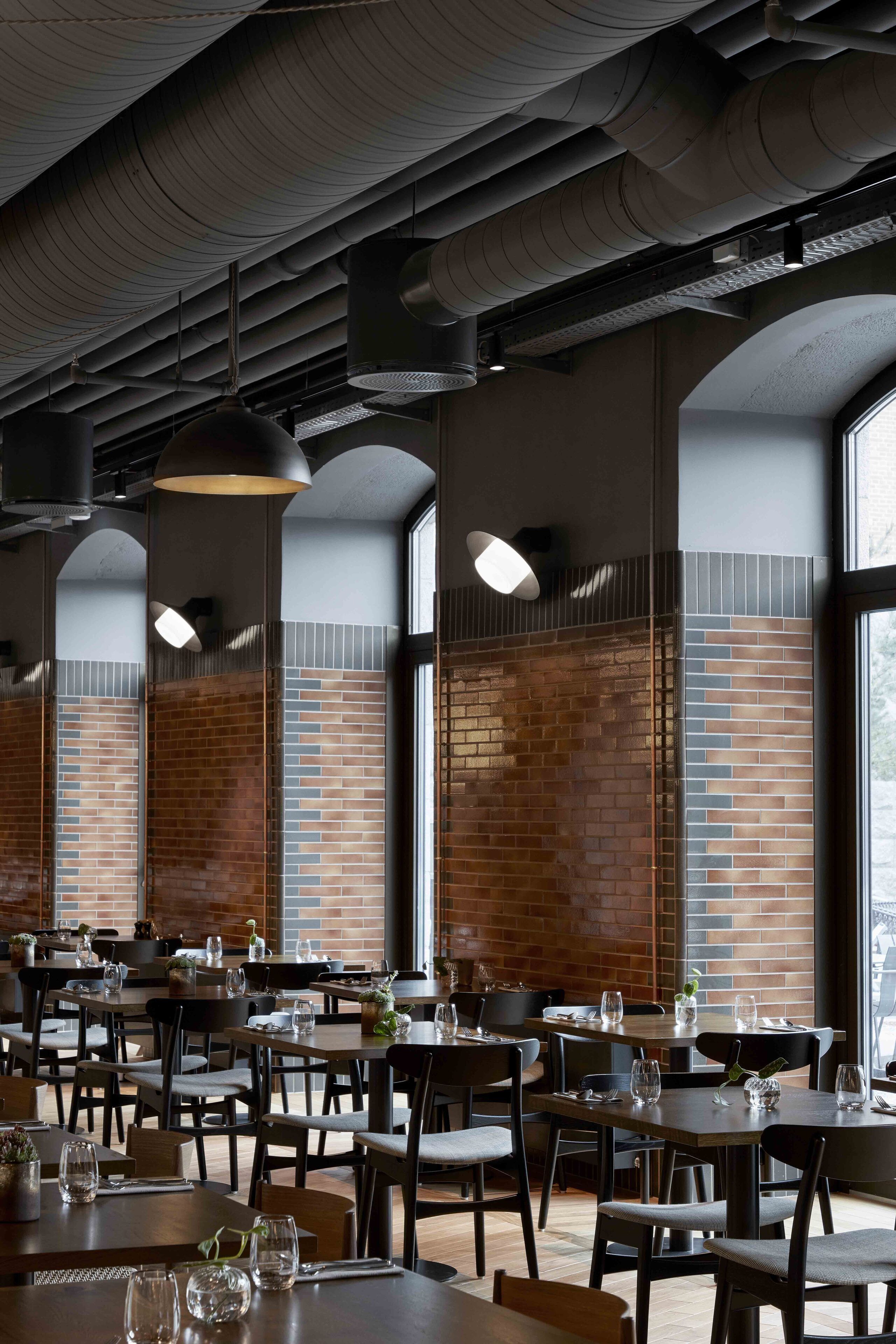 L’intérieur d’un restaurant avec des murs en briques, des tables en bois et des lampes suspendues.