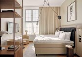 A modern hotel room with a bed, bedside table, lamp, and a large window.