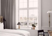 A hotel room with a large window, a bed, a desk, and a lamp.