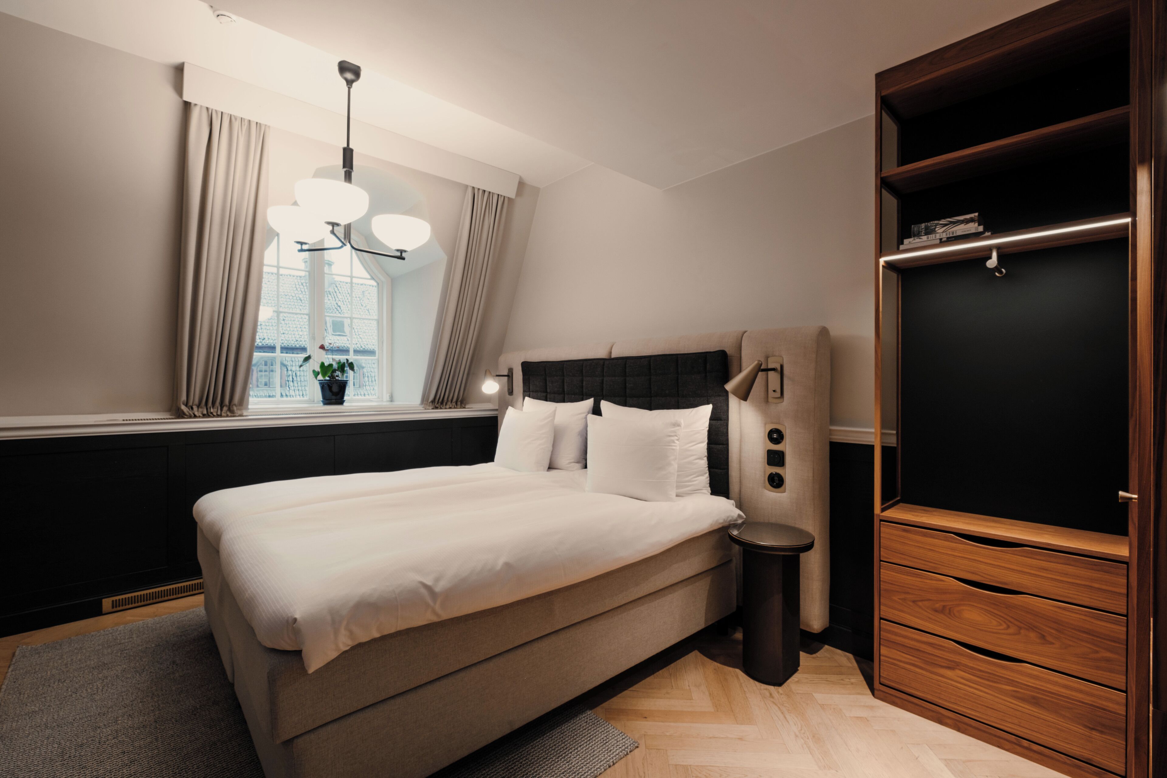 A modern bedroom with a large bed, a bedside table, a wardrobe, and a window with curtains.