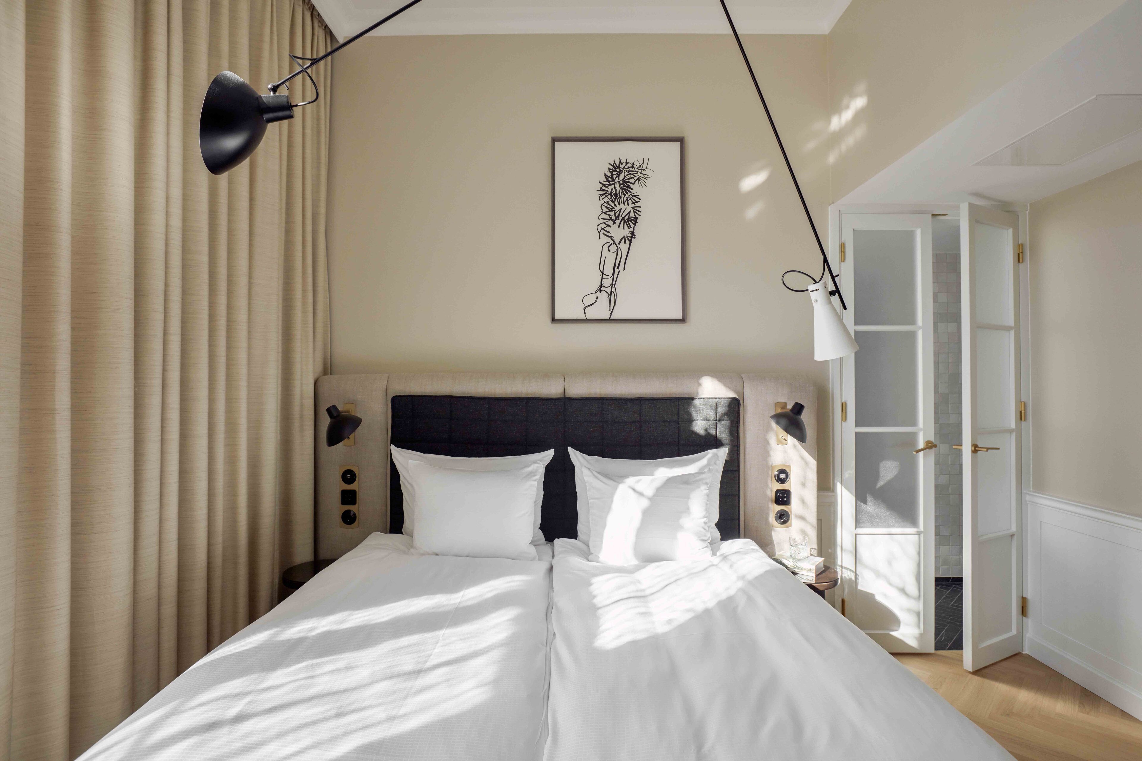 A neatly made bed with white linens, a black headboard, and a framed artwork on the wall.