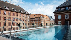 A swimming pool with metal railings, surrounded by brick buildings with multiple windows and balconies. - Villa Copenhagen (Copenhagen)