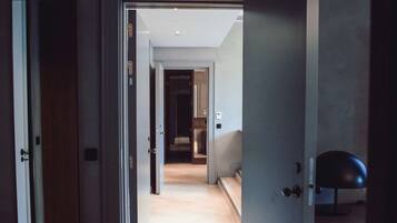 Un pasillo con suelo de madera, puertas abiertas que dan a otras habitaciones y una silla moderna en la esquina.
