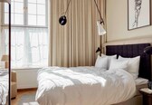 A bedroom with a large bed, a bedside table, a lamp, and a window with curtains.