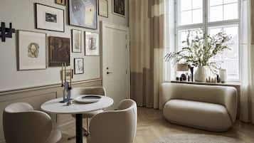 A modern living room with a round table, two chairs, a sofa, and a large window with curtains.