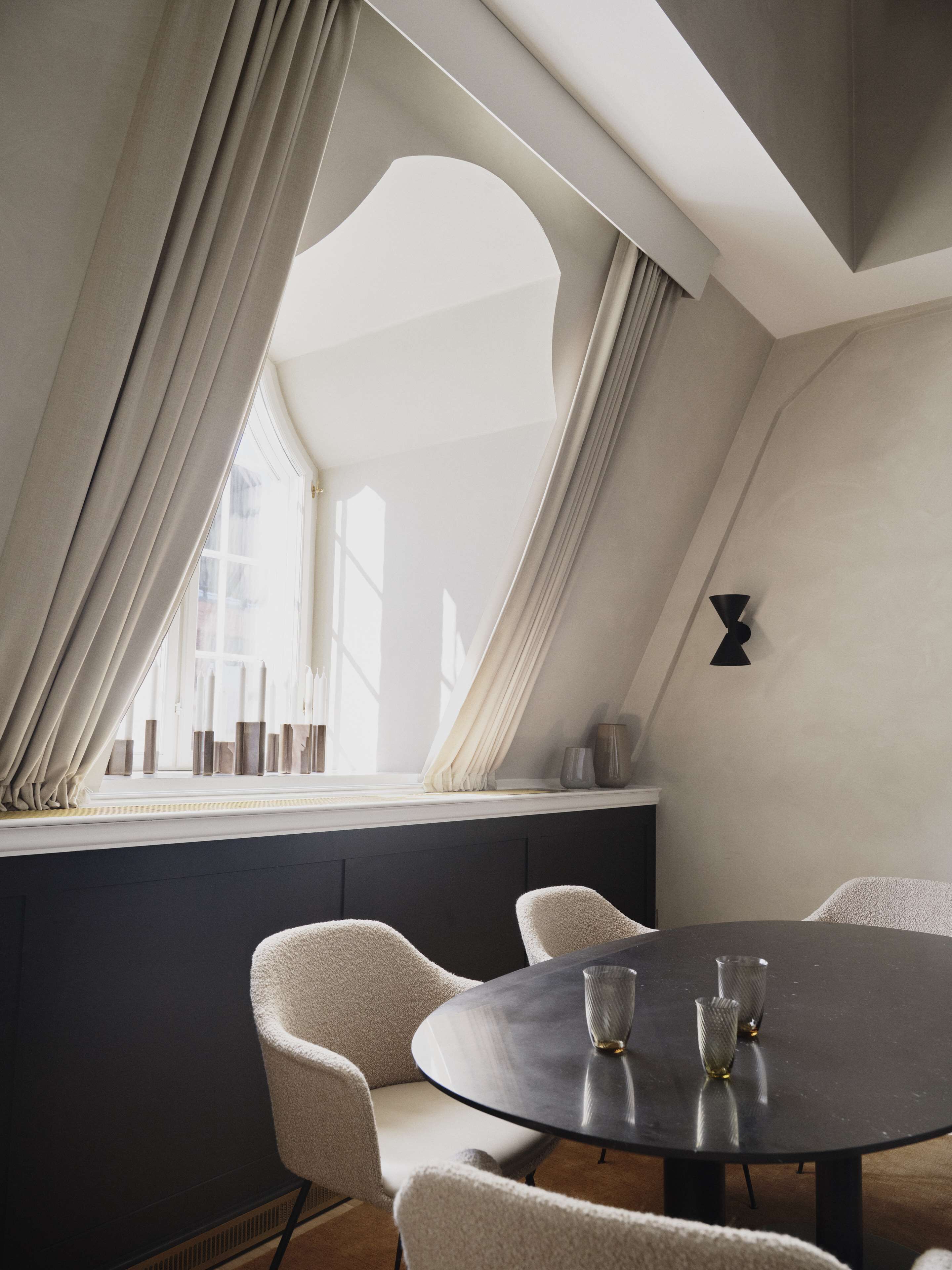 A modern dining area with a round table and four chairs, a large window with curtains, and a minimalist decor.