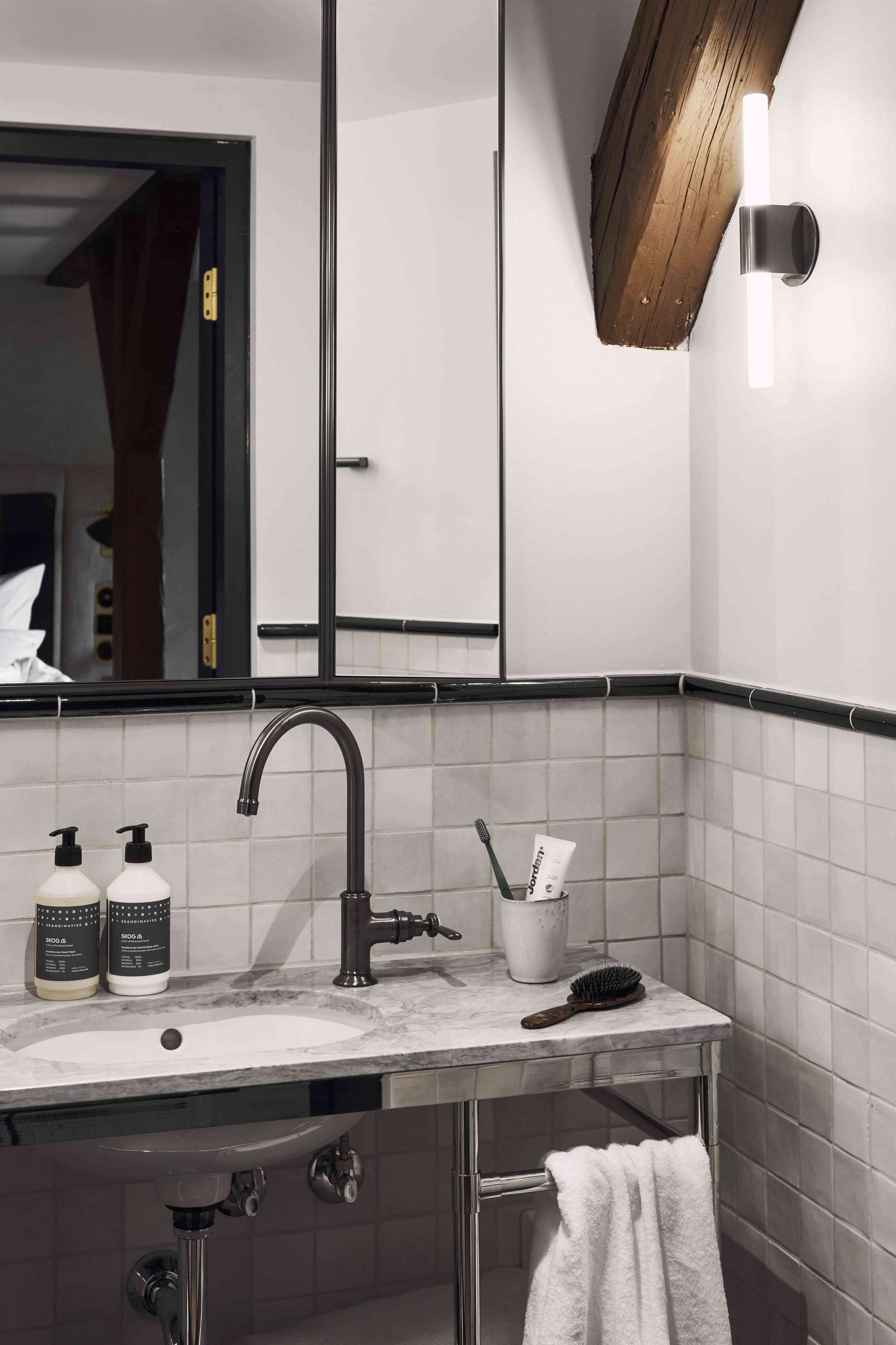 A modern bathroom with a marble sink, black faucets, a mirror, and a towel rack.