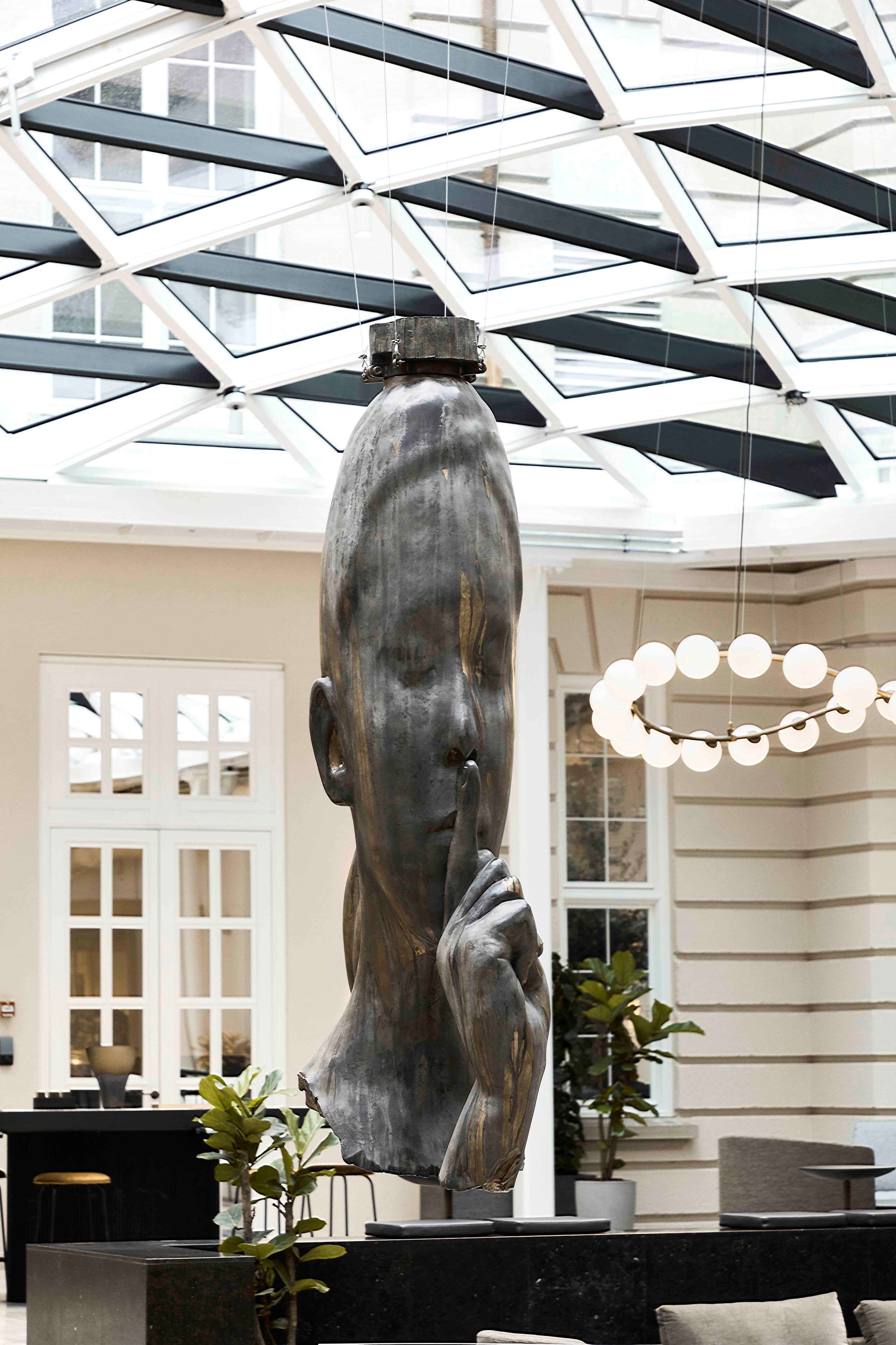En modern inredning med en stor skulptur av en mänsklig figur, ett glastak och en kristallkrona.