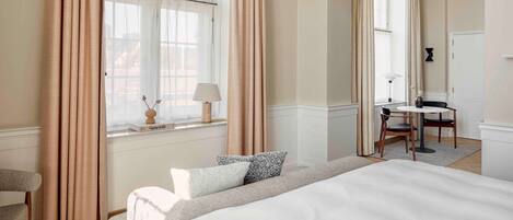A hotel room with a large bed, a desk with two chairs, a window with curtains, and a hanging lamp.