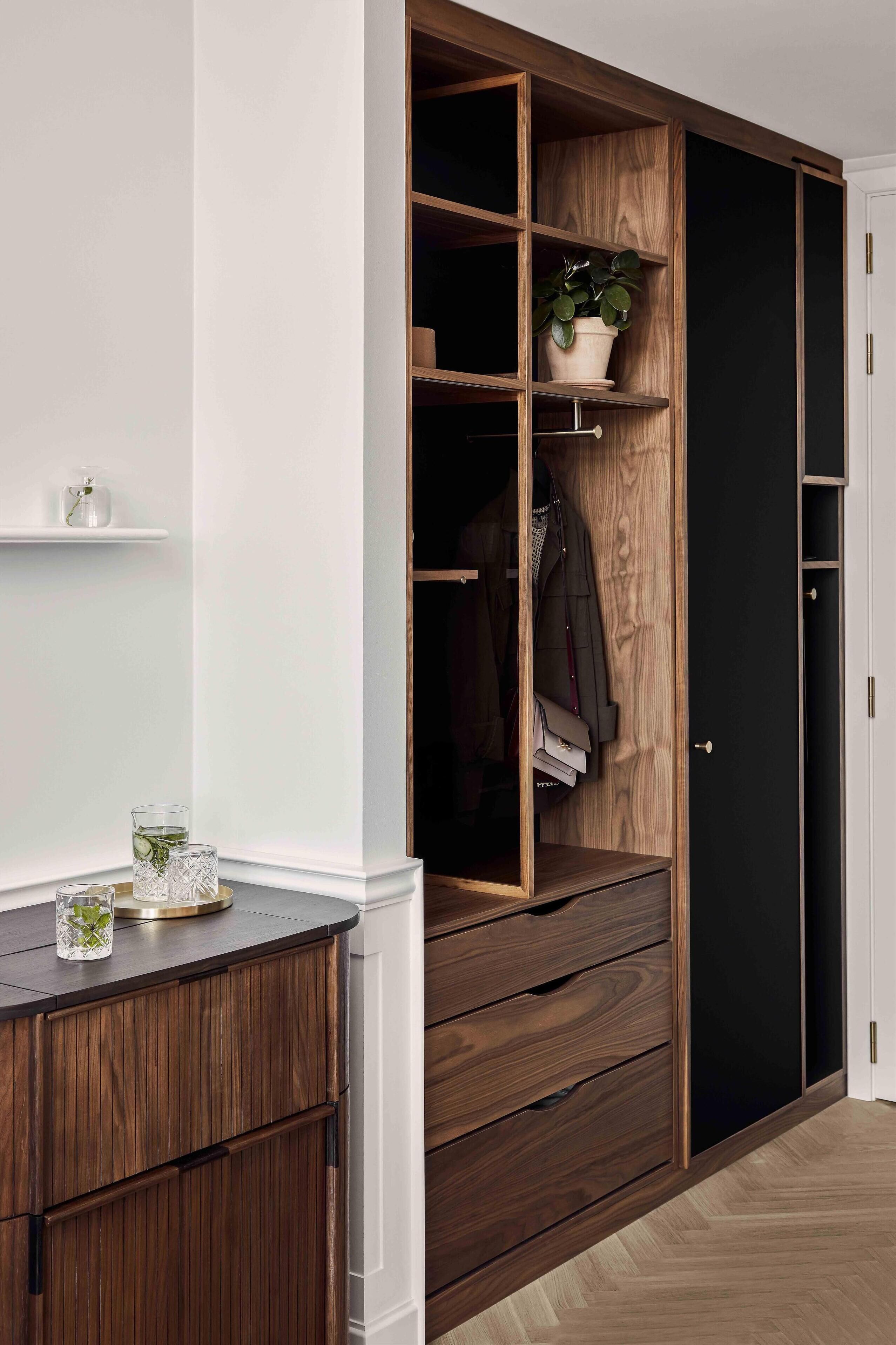 Un vestidor con estantes de madera, una planta en maceta y ropa colgada.