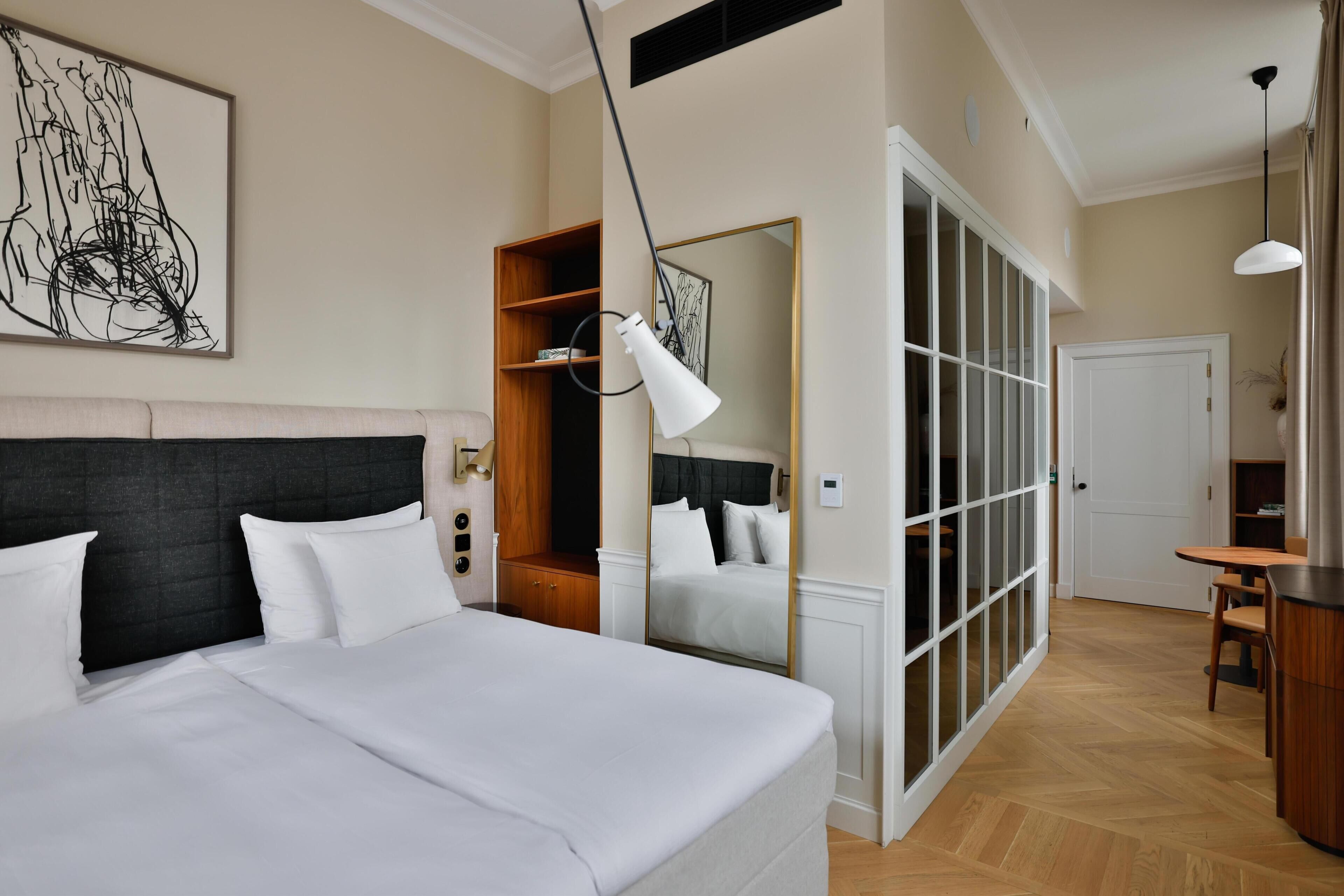 Una habitación de hotel con una cama grande, una mesita de noche, un espejo, un armario y un pequeño comedor.