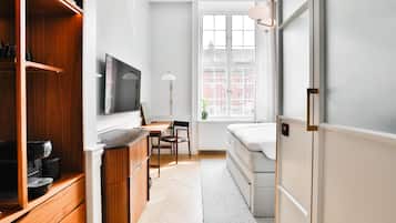 Habitación pequeña con cama, escritorio, televisión y ventana con vistas a edificios.