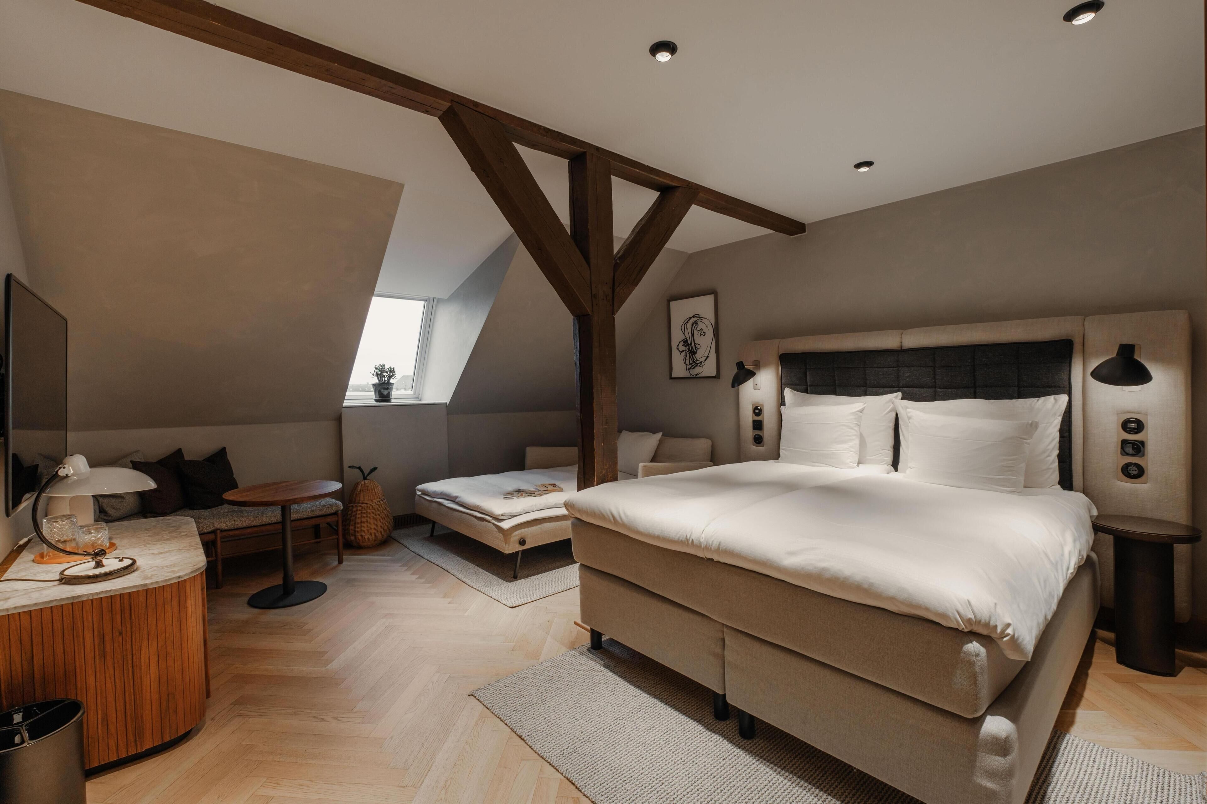 A bedroom with a large bed, a desk, a chair, and a small table.