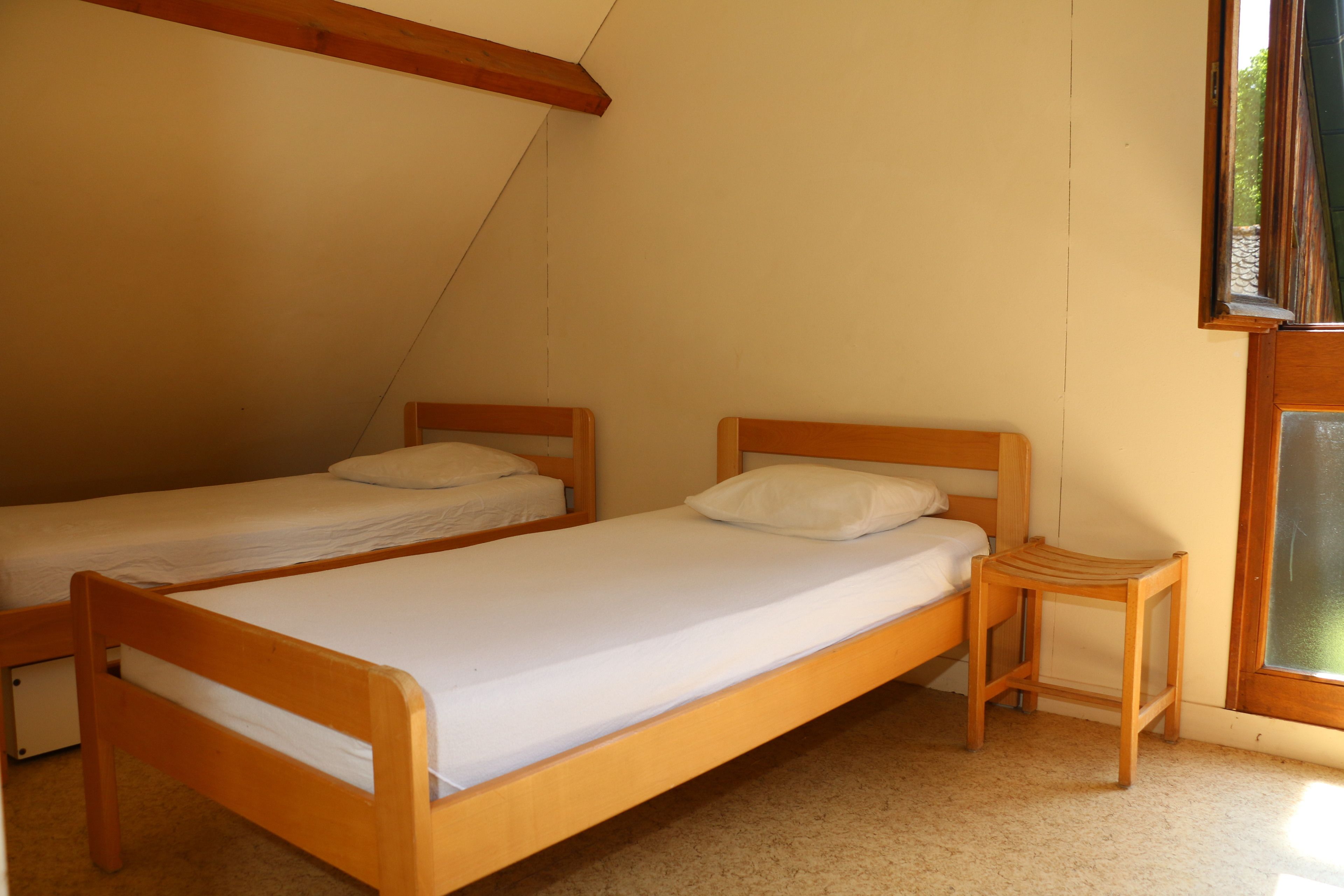 A room with two wooden beds, a small wooden nightstand, and a window with a view of greenery.