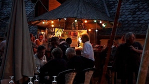 An outdoor dining area with tables and chairs, a thatched roof structure, and string lights. - Camping le Paisserou - Chalets (Najac)