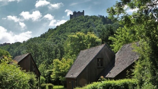 A rural setting with traditional wooden houses, a hill with a castle-like structure, and lush greenery. - Camping le Paisserou - Chalets (Najac)