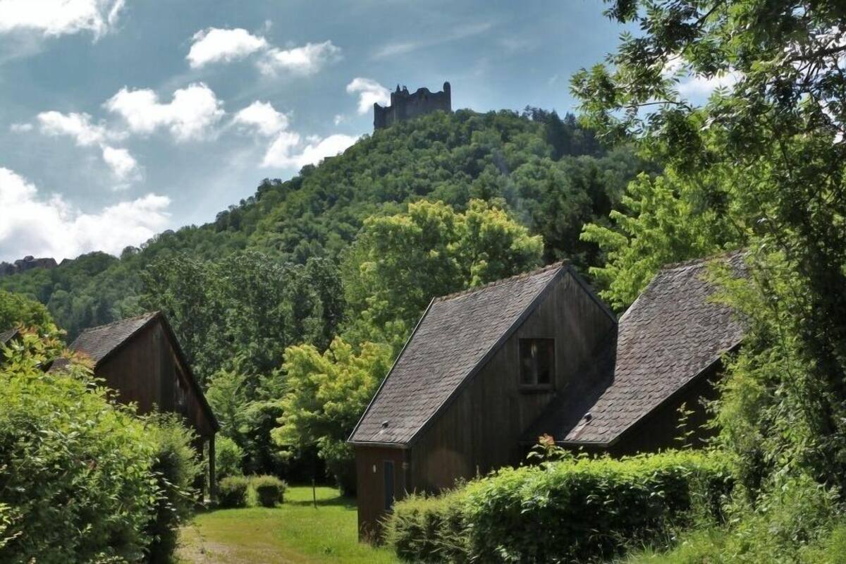 Un paysage rural caractérisé par des maisons traditionnelles en bois, une colline surmontée d’une structure ressemblant à un château, et une végétation luxuriante.