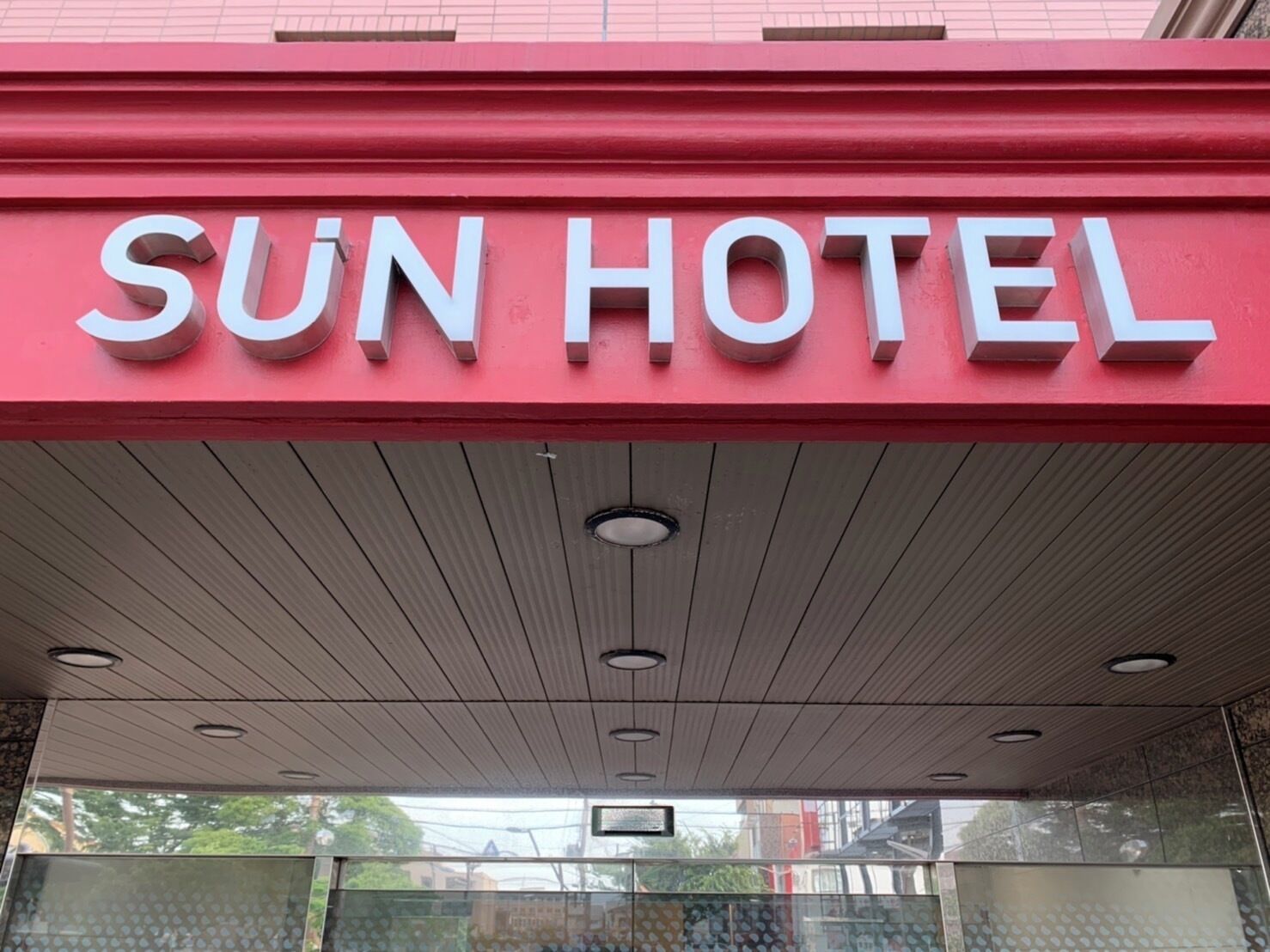 A hotel entrance with a red sign reading 'SUN HOTEL' and a modern ceiling design.