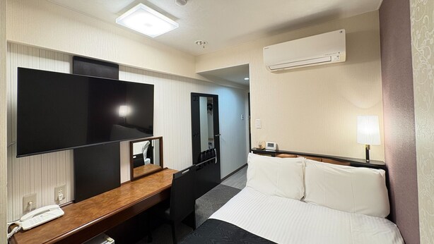 Quarto de hotel com cama, escrivaninha com telefone, televisão de tela plana, espelho, guarda-roupa e ar condicionado.